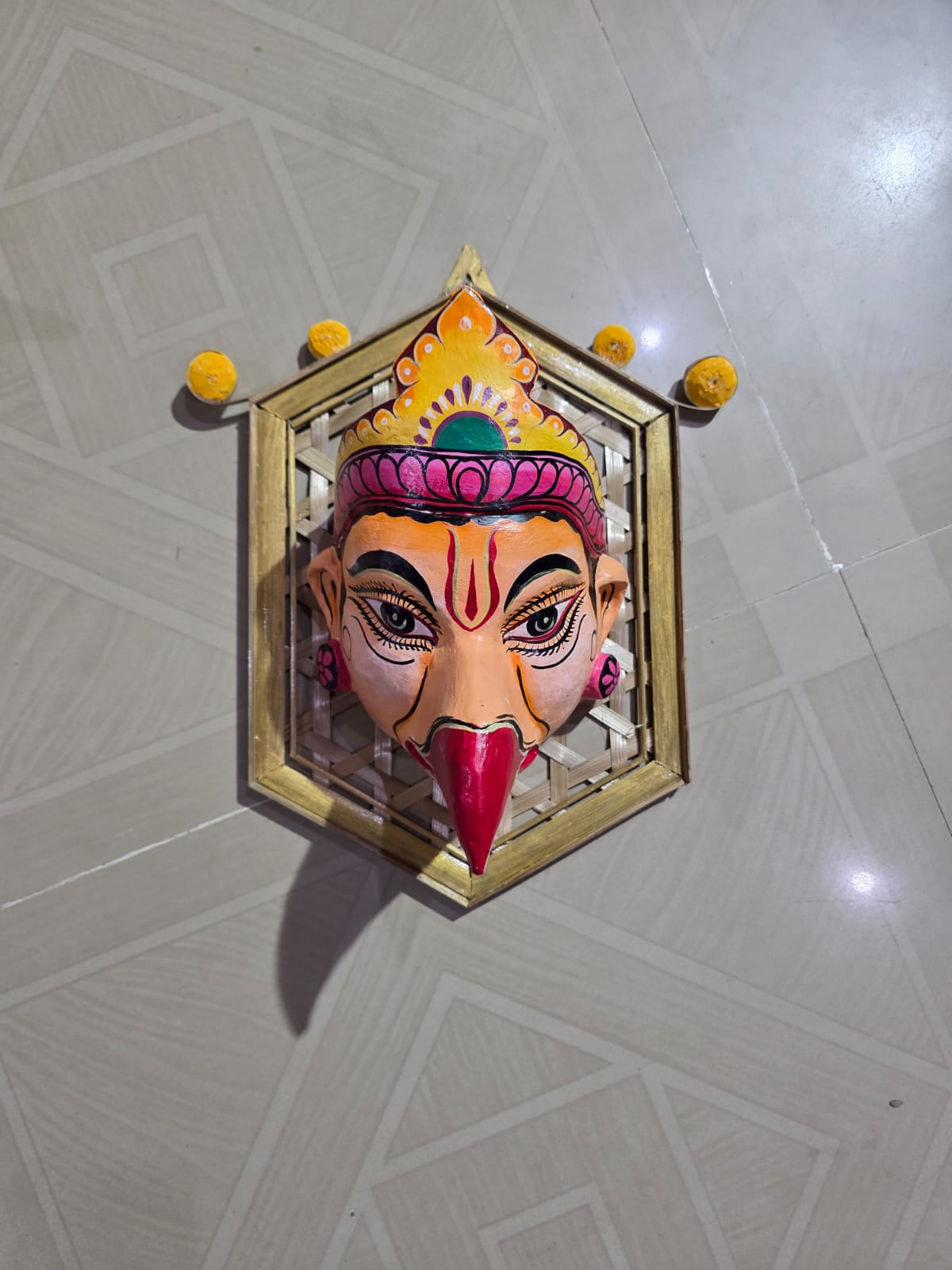 A hand-painted Garuda Sattriya mask with a golden crown, mounted on a woven bamboo frame