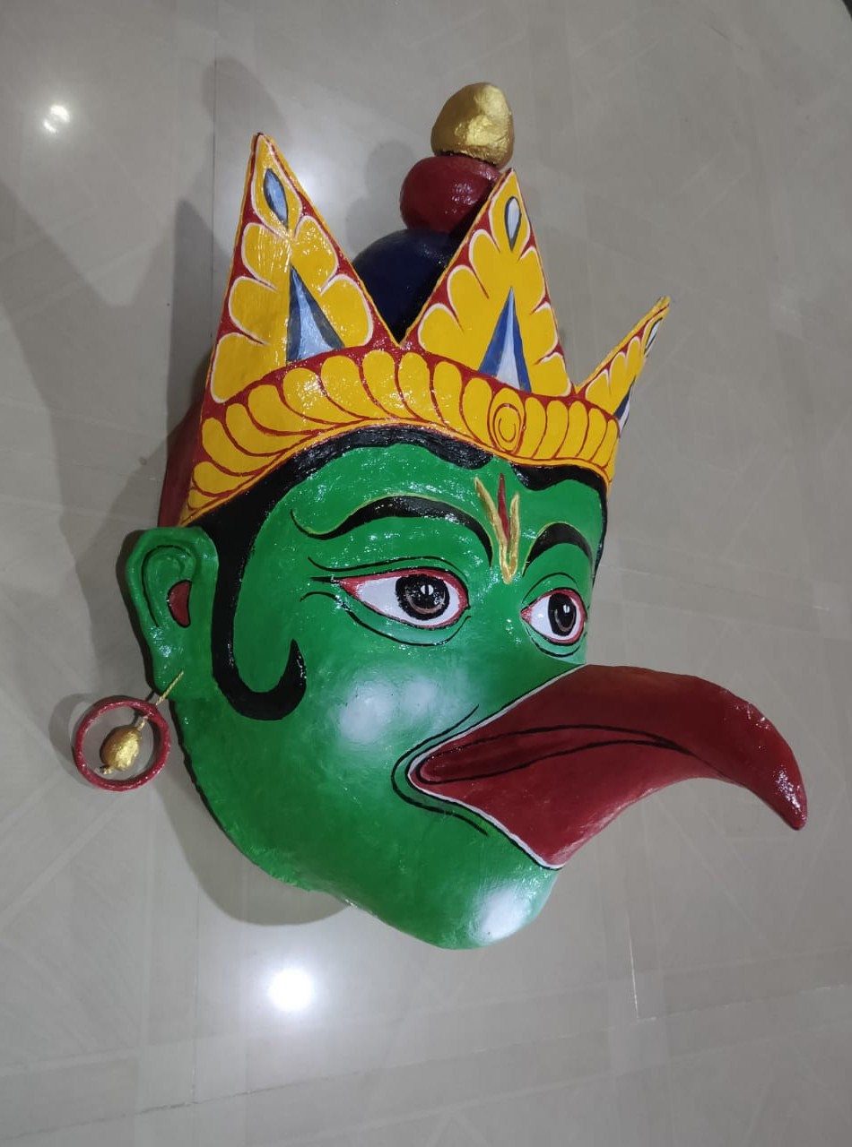 A green-faced bird mask with a red beak and golden crown