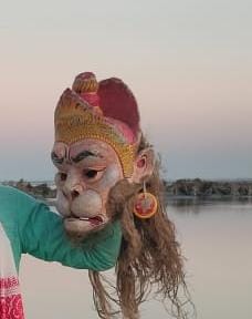 Performer wearing a Hanuman mask beside a river at dusk